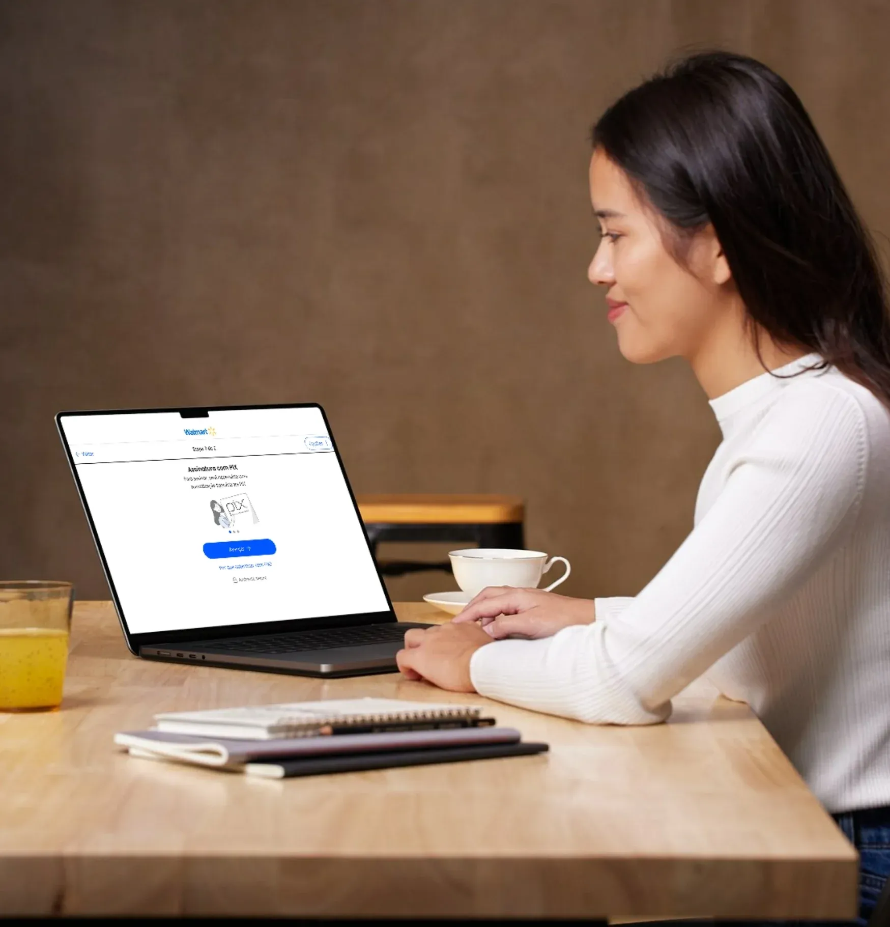 Mulher em uma mesa de café olhando a tela Assinatura com PIX em um notebook