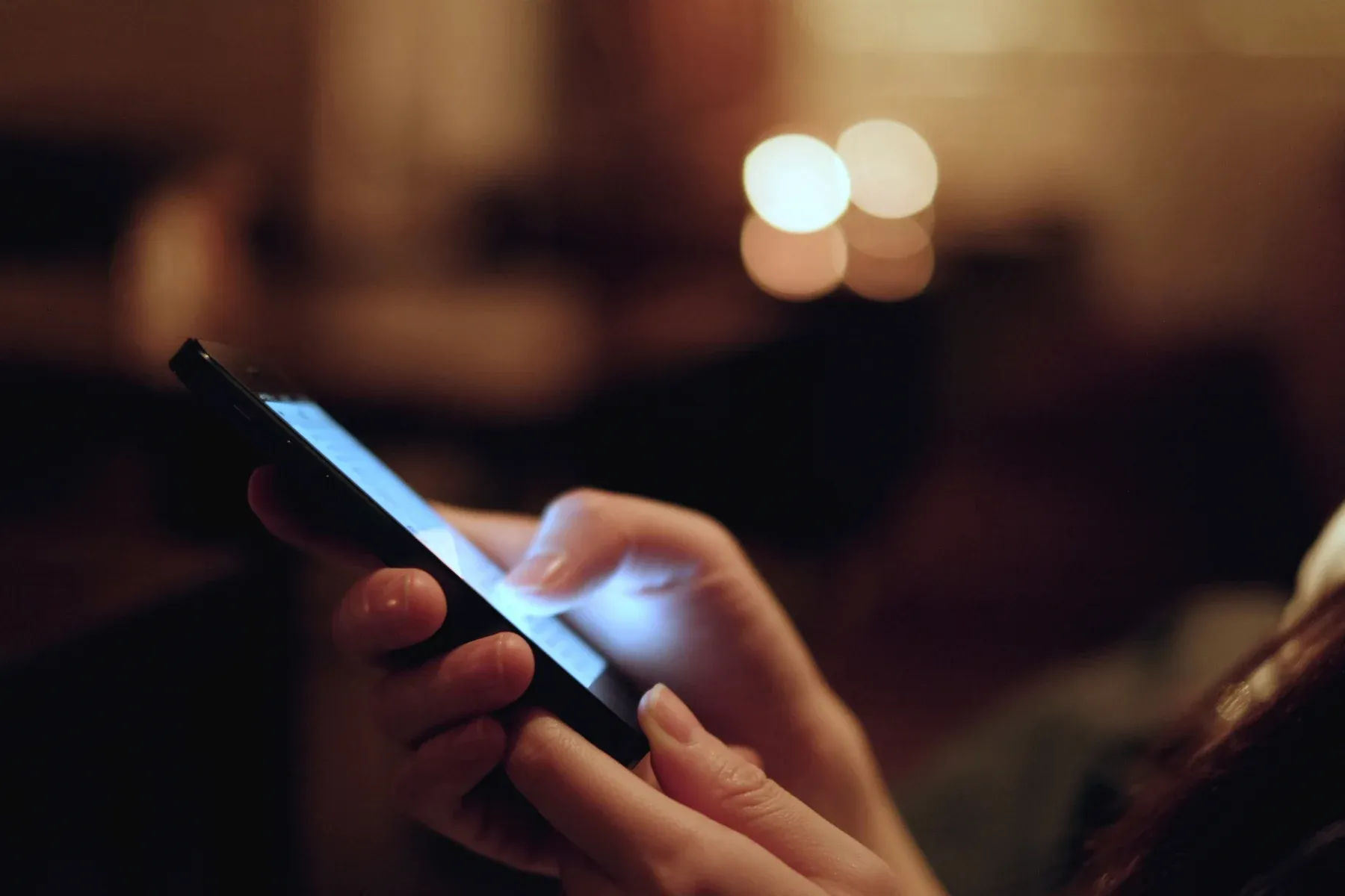 Mãos segurando um celular iluminado em um ambiente escuro